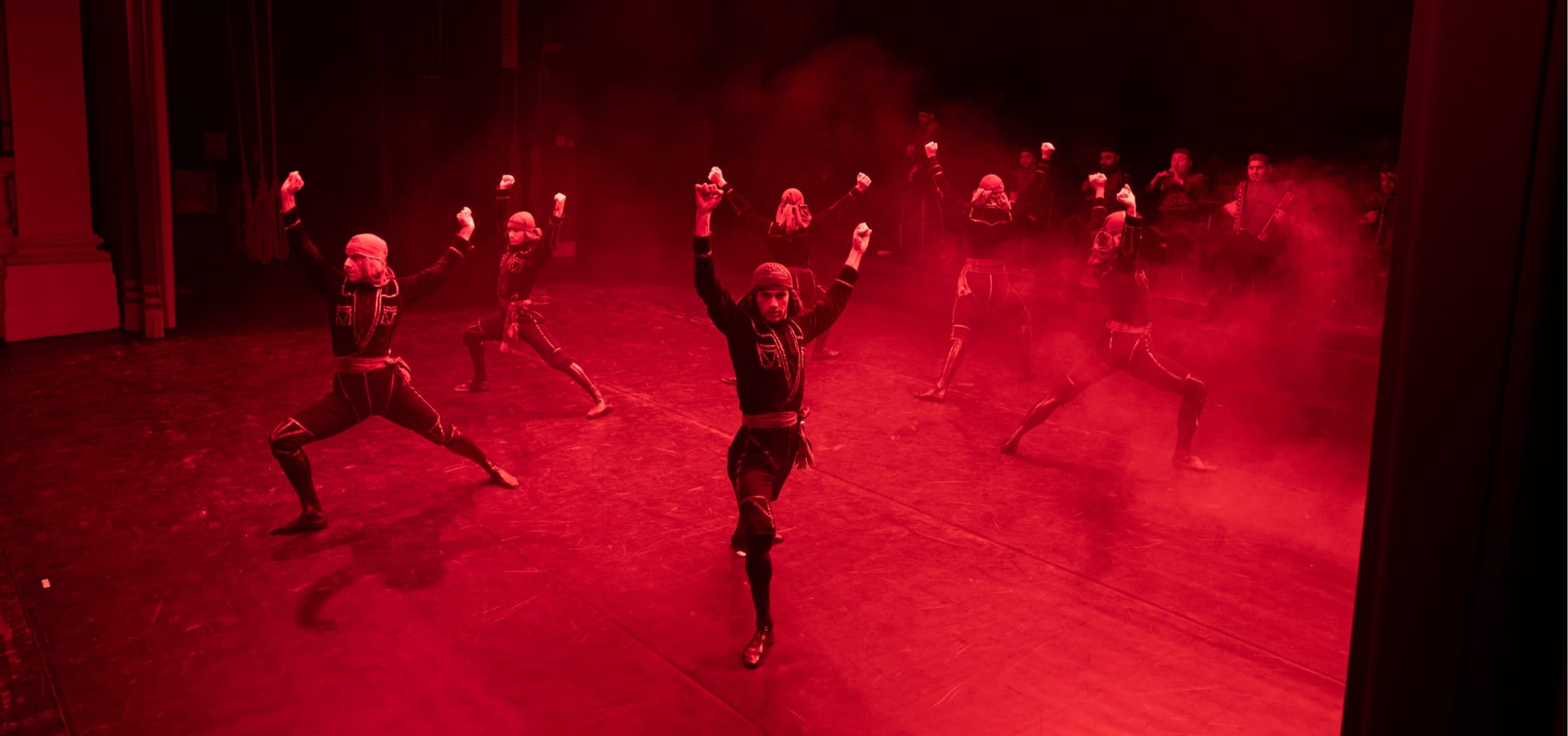 Dancers raising their fists on a stage filled with red smoke